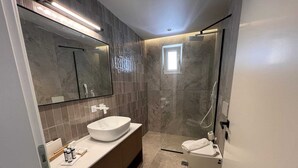 Et moderne badeværelse med et stort spejl, en skålhåndvask, en bruseniche og et toilet.