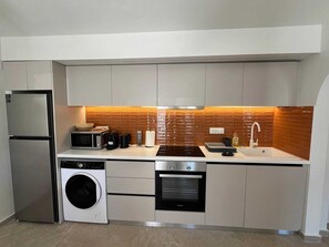A compact kitchen with a refrigerator, microwave, oven, washing machine, and a sink. - Ixia Cozyline Apartment- 101 (Rhodes)