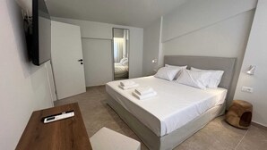 Et hotelværelse med en seng, et fjernsyn monteret på væggen, et træskrivebord og en lille træskammel.