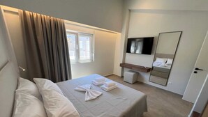 A hotel room with a bed, a TV, a mirror, and a window with curtains. - Ixia Cozyline Apartment- 102 (Rhodes)