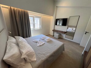 Ein Hotelzimmer mit Bett, Fernseher, Spiegel und einem Fenster mit Vorhängen.