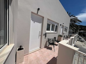 Ein Gebäude mit weißer Fassade, einer Tür, einem Fenster und einem kleinen Balkon mit Tisch und Stühlen sowie einem Blumentopf.
