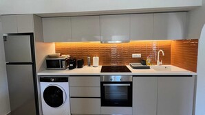 A compact kitchen with a built-in washing machine, a microwave, an oven, and a sink. - Ixia Cozyline Apartment- 102 (Rhodes)