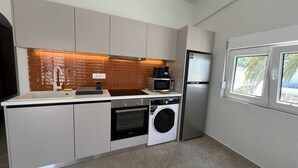 A compact kitchen with a washing machine, microwave, and a refrigerator. - Ixia Cozyline Apartment - 106 (Rhodes)