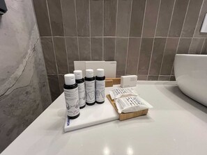 Ein Badezimmer mit weißem Waschtisch, einer weißen Toilette und einer Ausstattung an Pflegeprodukten, darunter Shampoo, Spülung und ein Dentalset.