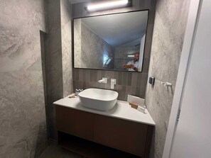 A bathroom with a large mirror, a white sink, and a marble wall. - Ixia Cozyline Apartments - 105 Studio (Rhodes)