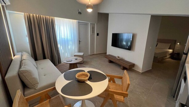 Ein modernes Wohnzimmer mit einer Couch, einem runden Esstisch, Korbstühlen, einem Fernseher und einer Bank.