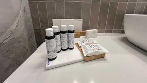 Ein Badezimmer mit weißem Waschtisch, einer weißen Toilette und einer Ausstattung an Pflegeprodukten, darunter Shampoo, Spülung und ein Dentalset.