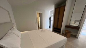 Ein modernes Hotelzimmer mit einem großen Bett, einer Holzbank, einem Spiegel und einem Kleiderschrank.