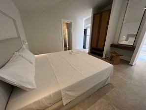 A modern hotel room with a large bed, a wooden bench, a mirror, and a wardrobe. - Ixia Cozyline Apartments - 105 Studio (Rhodes)