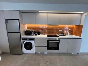A modern kitchen with a built-in washing machine, a microwave, and a stove. - Ixia Cozyline Apartment- 103 (Rhodes)