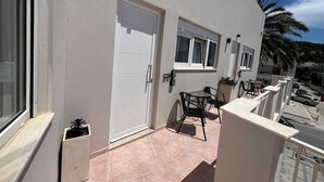 A building with a white exterior, a door, a window, a small balcony with a table and chairs, and a potted plant. - Ixia Cozyline Apartment - 104 (Rhodes)