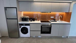 A modern kitchen with a built-in washing machine, a microwave, and a stove. - Ixia Cozyline Apartment - 104 (Rhodes)