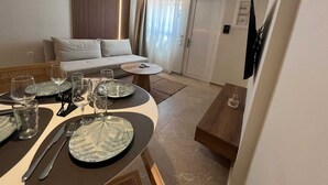 A dining area with a table set for four, a sofa, and a door with a security camera. - Ixia Cozyline Apartment - 104 (Rhodes)
