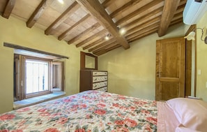Una camera da letto con soffitto in legno, copriletto floreale, comò e armadio in legno.