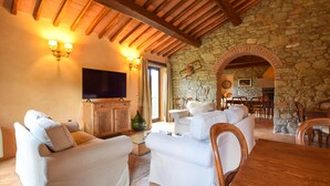 A cozy living room with a stone wall, wooden ceiling beams, a flat-screen TV, and a dining area with chairs and a table. - Beautiful home in Monte Santa Maria Tibe (Monte Santa Maria Tibe)
