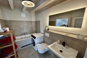 A modern bathroom with a washing machine, a sink, and a mirror.