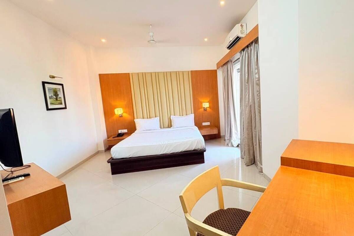 A hotel room with a bed, bedside tables, a desk, a chair, and a television.