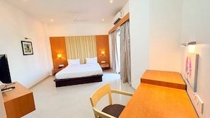 A hotel room with a bed, bedside tables, a desk, a chair, and a television. - Imperial Tamanna Hotel  (Pimpri-Chinchwad)