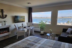 A modern room with a large window, a fireplace, a dining area, and a sofa. - Holiday apartment with 1 bedroom (Fehmarn OT Burgtiefe)