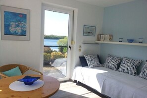 Ein Zimmer mit einem Bett, einem Sessel, einem Tisch und Blick auf ein Gewässer.