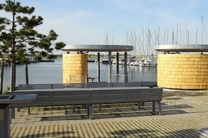 A waterfront park with benches, a wooden fence, and a view of boats. - Trumann "Laughing Gull" (Fehmarn (Südstrand))
