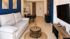 A modern living room with a sofa, a coffee table, a TV, and artwork on the walls. - Apartment for 3, a short walk from the beaches (Roquetas de Mar)