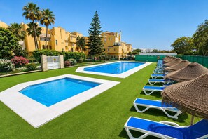 Ein Poolbereich mit zwei rechteckigen Pools, grüner Kunstrasen und Liegestühlen mit Sonnenschirmen.