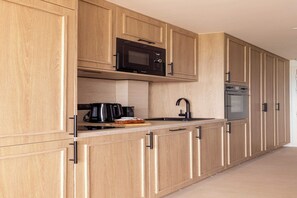 Eine moderne Küche mit Holzausstattung, einer Mikrowelle, einer Kaffeemaschine und einem Backofen.