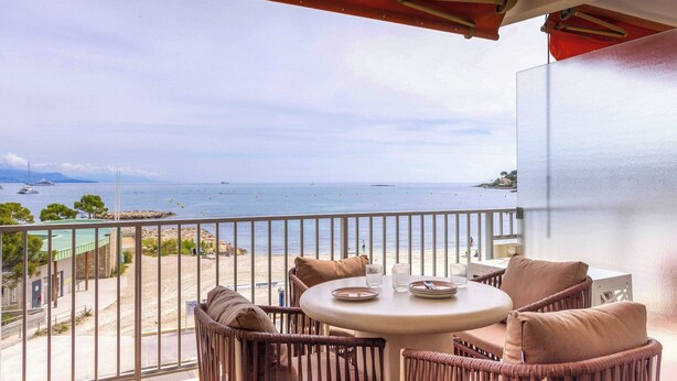 A balcony with wicker furniture, a round table, and a view of the sea and beach. - 1BDR/4P flat with stunning sea views (Antibes)