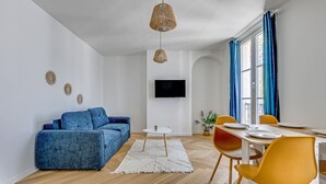 Una sala de estar moderna con un sofá azul, una mesa de comedor con sillas amarillas, una alfombra blanca y un televisor de pantalla plana montado en la pared.