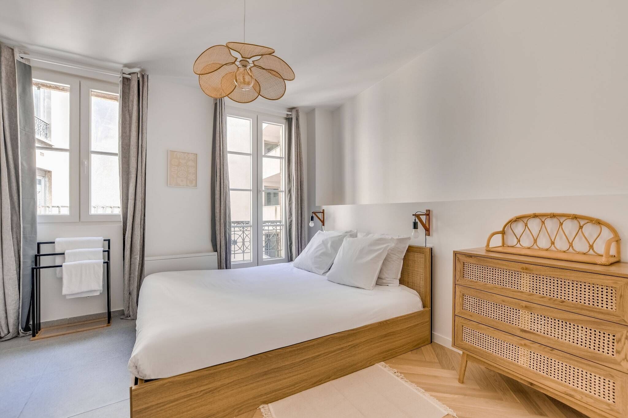 Een slaapkamer met een bed, een rotan dressoir, een hanglamp en een raam met gordijnen.