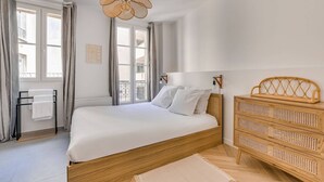 Un dormitorio con una cama, un aparador de ratán, una lámpara colgante y una ventana con cortinas.