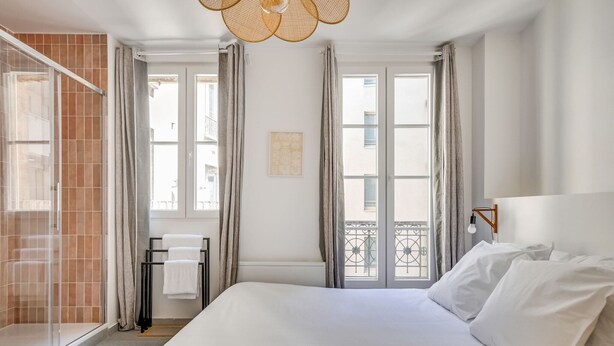 Habitación de hotel con cama, ventana con cortinas, toallero y vistas al balcón.