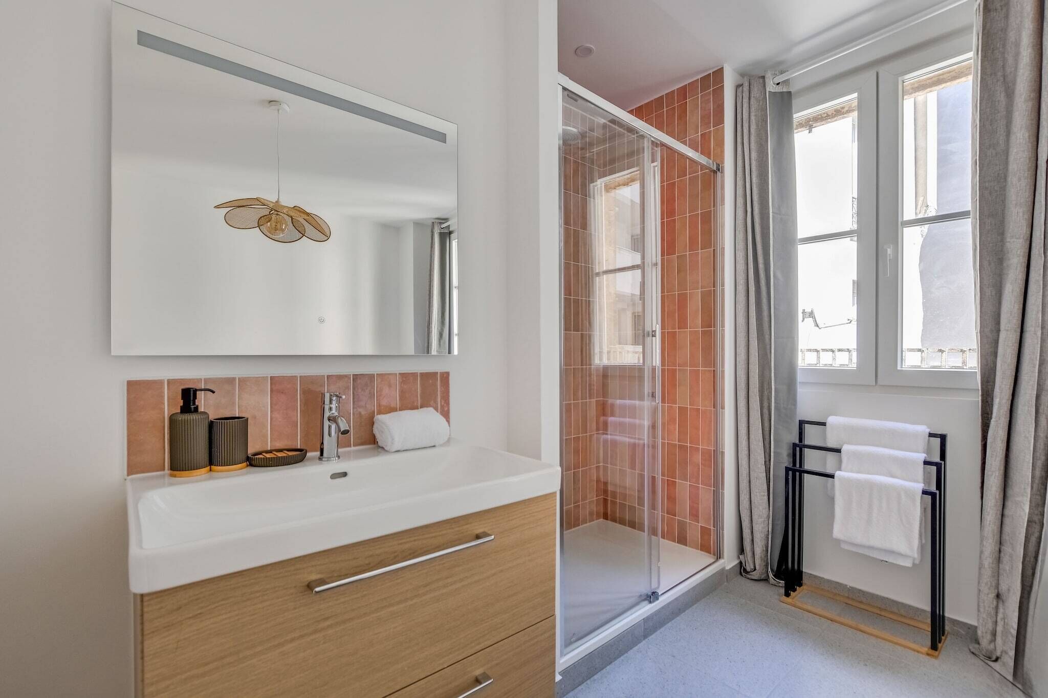 Une salle de bain moderne avec un grand miroir, une cabine de douche, un porte-serviettes et une fenêtre avec des rideaux.