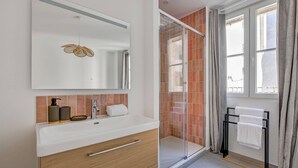 Un baño moderno con un espejo grande, cabina de ducha, perchero y una ventana con cortinas.