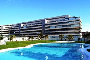 Ein mehrstöckiges Hotel mit Schwimmbad, umgeben von Grünflächen und Palmen.