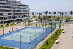 Ein mehrstöckiges Hotel mit Tennisplatz, Palmen und Blick auf den Ozean.