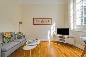 Ein modernes Wohnzimmer mit grauem Sofa, Couchtisch, Fernseher und einem gerahmten Kunstwerk an der Wand.