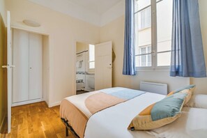 Una camera da letto con un letto, un armadio, una finestra con tende e un bagno visibile attraverso una porta aperta.