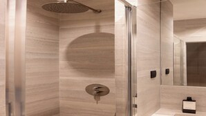 Un baño moderno con cabina de ducha de vidrio, pared de mármol y una pequeña zona de lavabo.