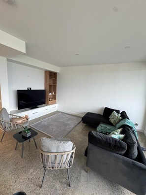 Ein modernes Wohnzimmer mit Flachbildfernseher, einer Couch, einem Sessel und einem Couchtisch.
