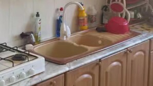 A kitchen with wooden cabinets, a double sink, a gas stove, and various kitchen items.