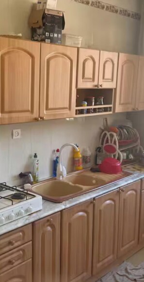A kitchen with wooden cabinets, a double sink, a gas stove, and various kitchen items on the countertop. - Bed and breakfast bejaia (Béjaïa)
