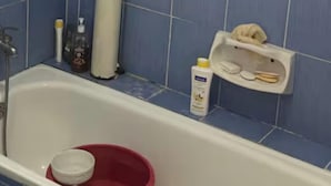 A bathroom with blue tiles, a white bathtub, a red bucket, and toiletries on the wall.