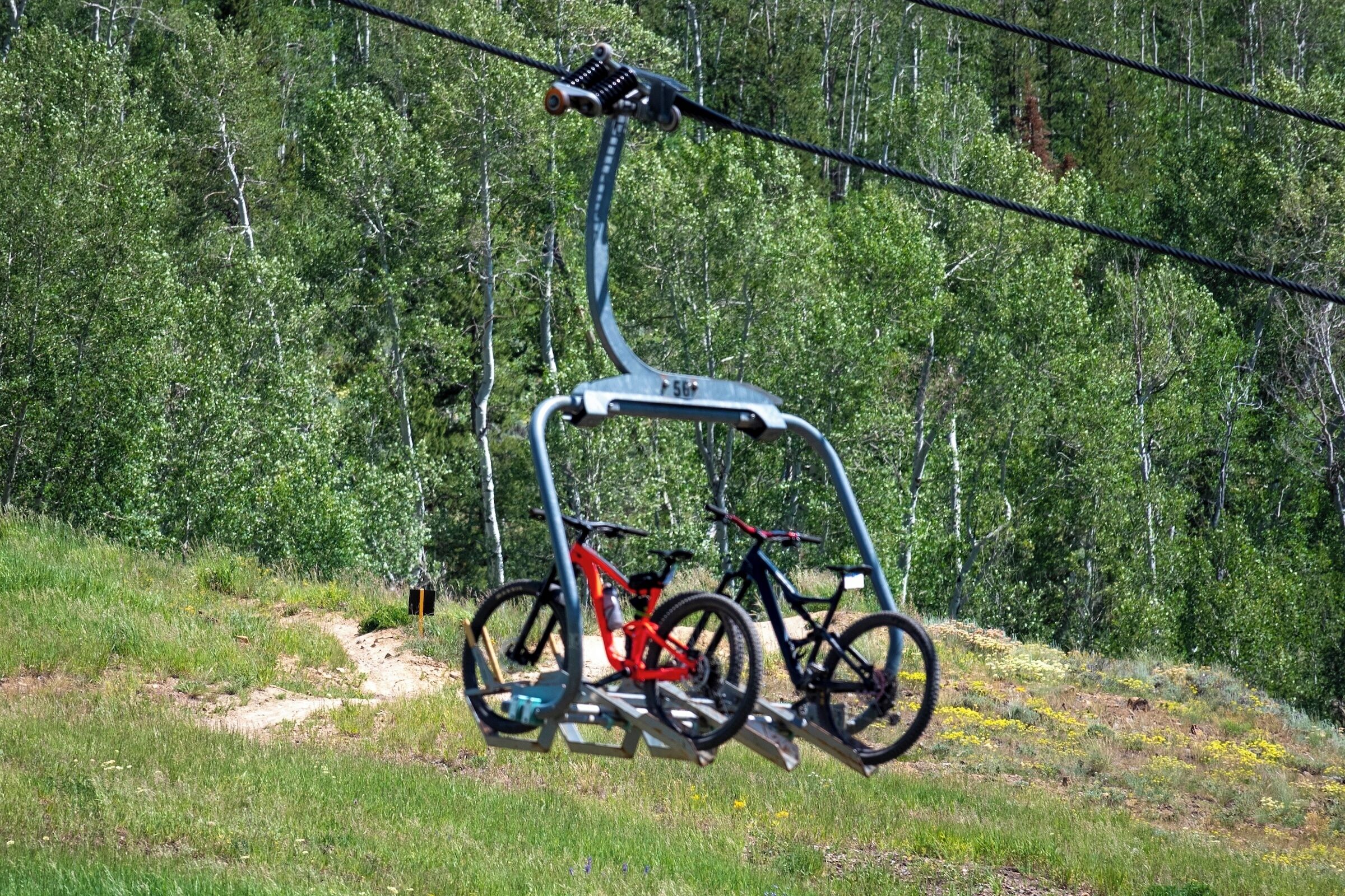 Un télésiège auquel sont attachés deux vélos, avec une forêt en arrière-plan.