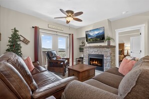 Ein Wohnzimmer mit Kamin, Ledersofas, Deckenventilator und Blick durch eine Glastür.
