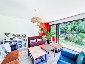 Un salon moderne comprenant un canapé, une table basse et des fauteuils, une bibliothèque et une grande fenêtre donnant sur un paysage verdoyant.