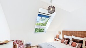 A bedroom with a skylight, a bed with multiple pillows, a bedside table with a lamp, and a small stool. - Maison de Kermamas by Interhome (Sarzeau)
