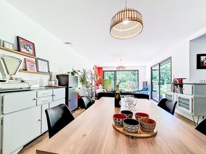 Un espace de salle à manger moderne avec une table en bois, des chaises, un luminaire suspendu et une vue dégagée grâce à de grandes fenêtres.